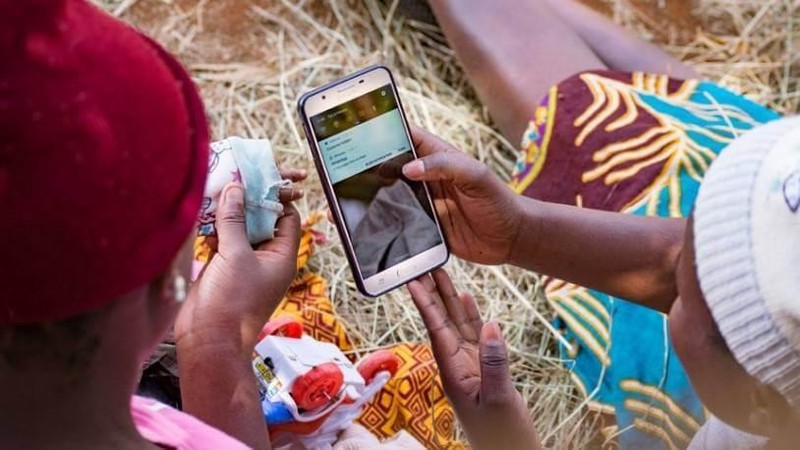 Watu wawili wakiwa wamekaa nje wakitazama simu ya mkononi, wakionyesha matumizi ya huduma ya malipo au mchezo mtandaoni.