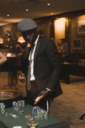 Mwanaume aliyevaa vizuri akiwa amesimama karibu na meza ya kasino, akishika chips za kucheza katika mazingira ya ndani ya kasino.