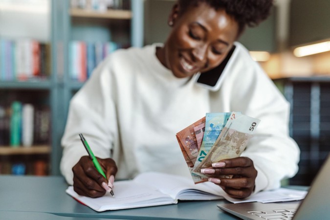 Mwanamke akihesabu pesa huku akiandika kwenye daftari na simu karibu.