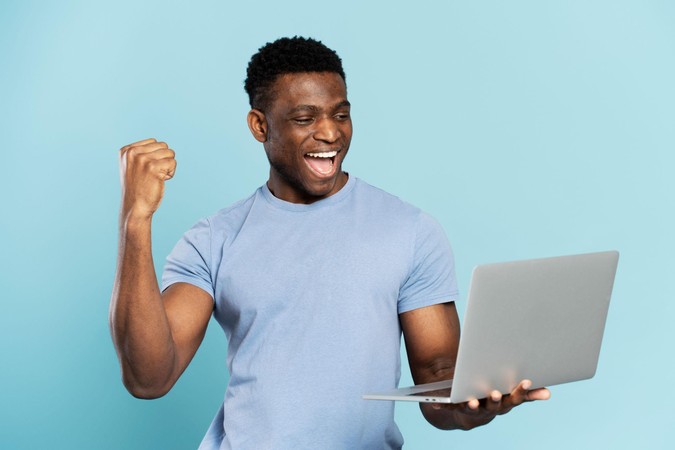Mwanaume akishangilia akiwa na laptop, ishara ya ushindi mkubwa.