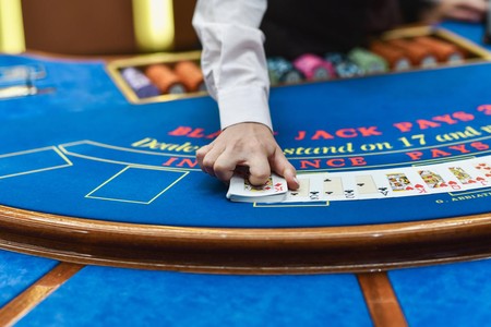 Mkono wa dealer unavuta kadi juu ya meza ya blackjack ya buluu ndani ya kasino.