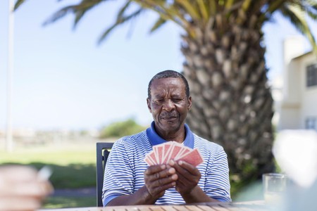 Mwanaume mzee amekaa nje akiwa ameshika kadi mkononi karibu na mtende.
