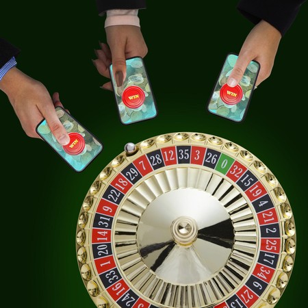 Mikono mitatu imeshika simu zenye kitufe cha WIN juu ya picha ya gurudumu la roulette.