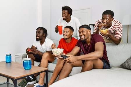 Kikundi cha vijana weusi wamekaa sebuleni wakicheza mchezo wa video huku wakila vitafunio na kunywa.