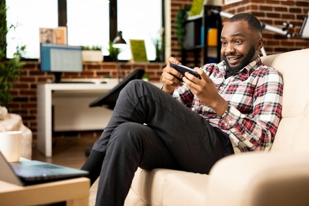 Mwanaume amekaa kwenye sofa akicheza au kutazama kitu kwenye simu akiwa na tabasamu.