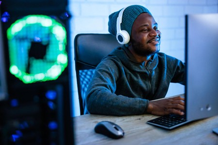Mwanaume amekaa mbele ya kompyuta akiwa na headphones katika chumba chenye mwanga wa bluu.
