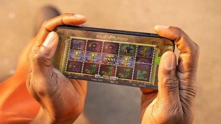 Mikono imeshika simu inayocheza mchezo wa slot kwenye skrini.