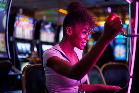 Mwanamke anacheza mashine ya slot ndani ya kasino yenye taa za rangi nyingi.