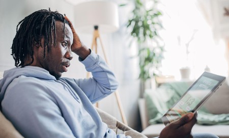 Mwanaume anaonekana kushtuka huku akiangalia tablet akiwa ameketi sebuleni nyumbani.