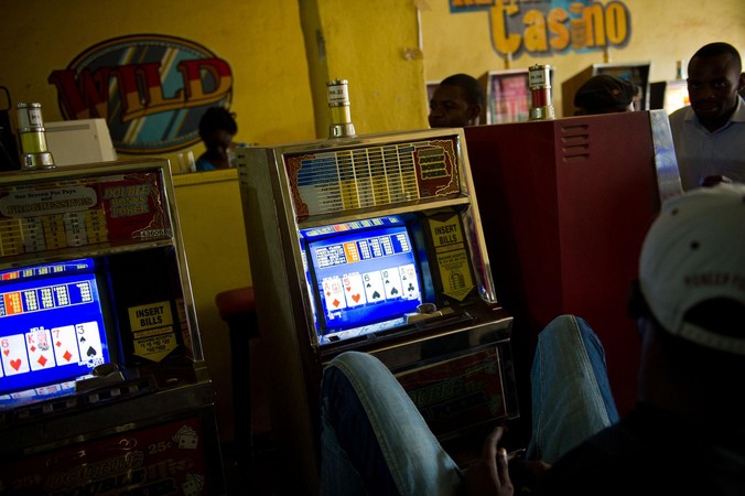 Watu wanacheza mashine za slot ndani ya ukumbi wa casino wenye mwanga hafifu.