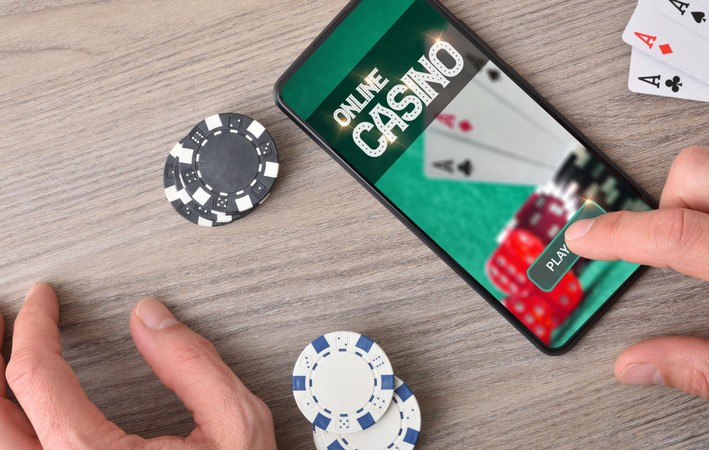 Simu inaonyesha maandishi ya Online Casino na kitufe cha Play, huku mezani kukiwa na chipsi na kadi za kucheza.