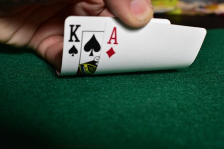 Mkono unafunua taratibu kadi mbili juu ya meza ya kijani ya casino katika tukio la karibu la mchezo wa karata.