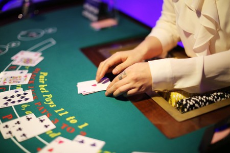 Mtoaji wa mchezo mezani anaweka kadi juu ya meza ya blackjack yenye chips na alama za mchezo chini ya mwanga wa casino.