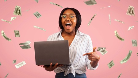Mwanamke mwenye furaha ameshika laptop huku noti za dola zikionekana kuruka angani.