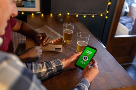 Watu wawili wakiwa mezani baa wanatazama simu yenye programu ya casino online.