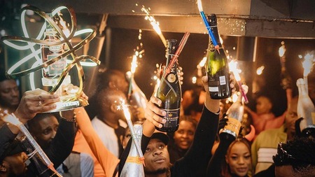 Umati wa watu kwenye sherehe ya usiku wakinyanyua chupa za champagne na cheche za fataki.